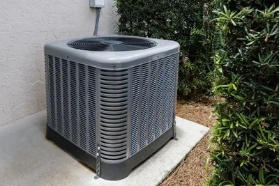 Residential air conditioning condenser on a concrete pad beside a home