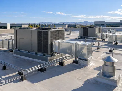 Commercial rooftop HVAC unit with ductwork on an office building, with mountains in the distance